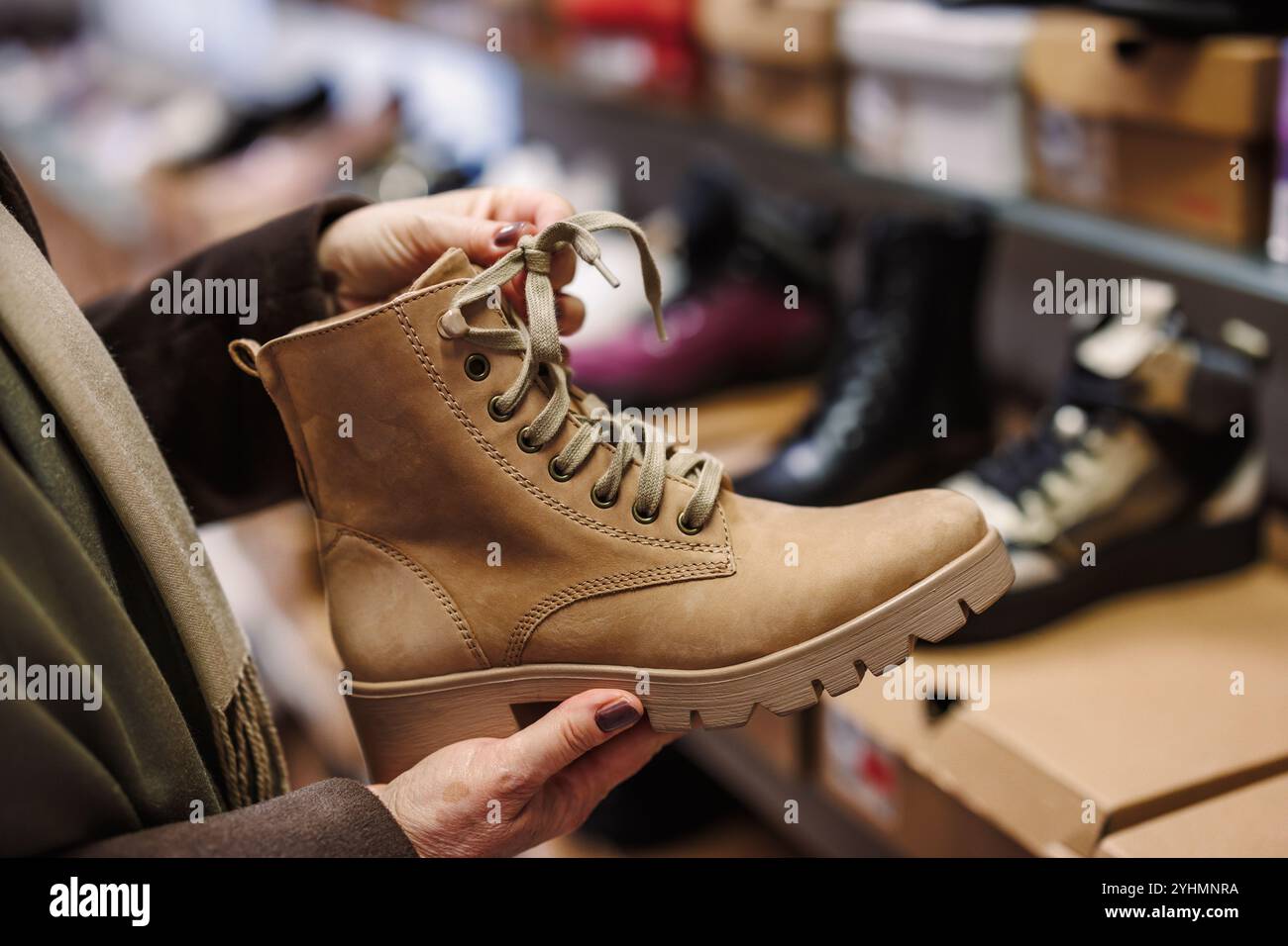 La femme choisit et achète des bottines en cuir élégantes dans le magasin de chaussures. Shopping chaussures tendance Banque D'Images