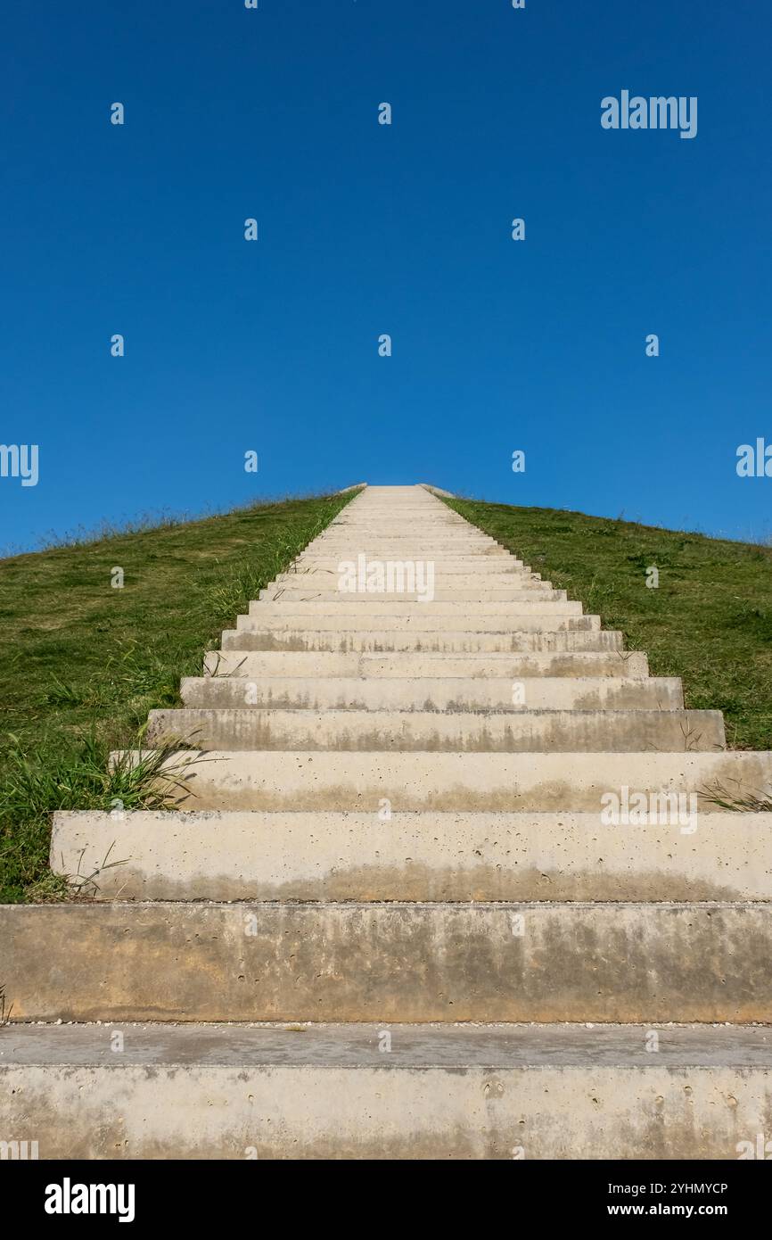 Long escalier menant à une colline verte sous Blue Sky. Marches en béton menant à une colline herbeuse par une journée ensoleillée. Photo verticale. Personne, copiez l'espace pour Banque D'Images