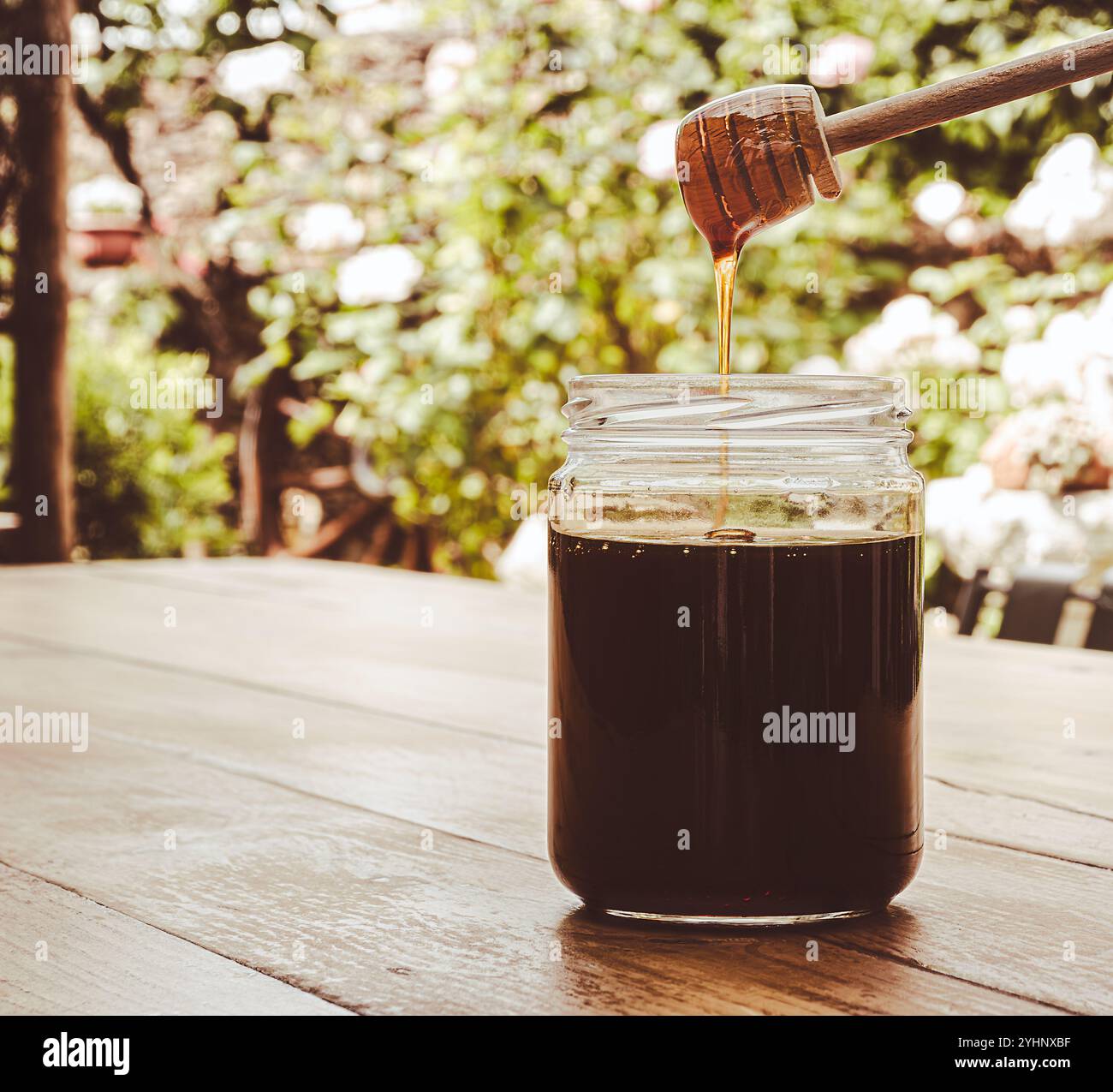 Pot en verre avec du miel et un distributeur en bois sur une table un fond flou. Banque D'Images