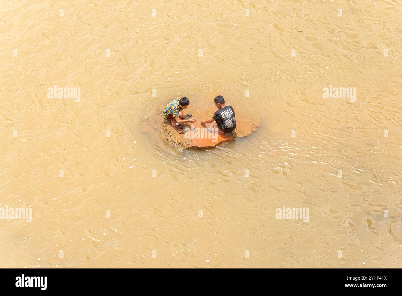 Xepon, Laos - 23 juin 2023 : deux garçons jouent sur un rocher entouré d'eau dans la rivière Banghiang. Un garçon porte un T-shirt avec une impression du film Joker (2019) Banque D'Images