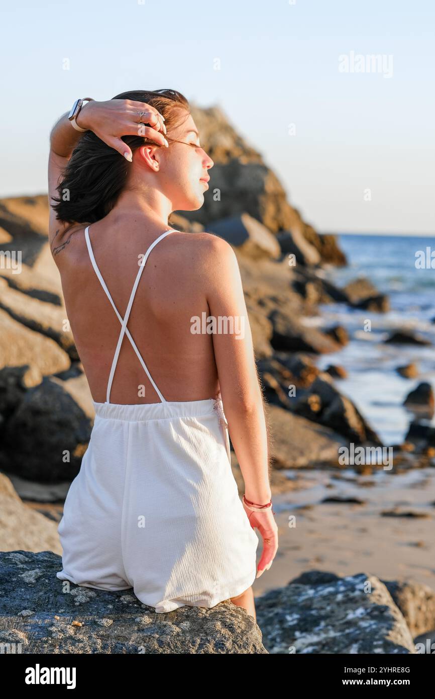 Portrait d'une femme aux cheveux bruns courts sur fond de côte rocheuse au Portugal. Tranquillité, coucher de soleil et harmonie avec la nature. Banque D'Images