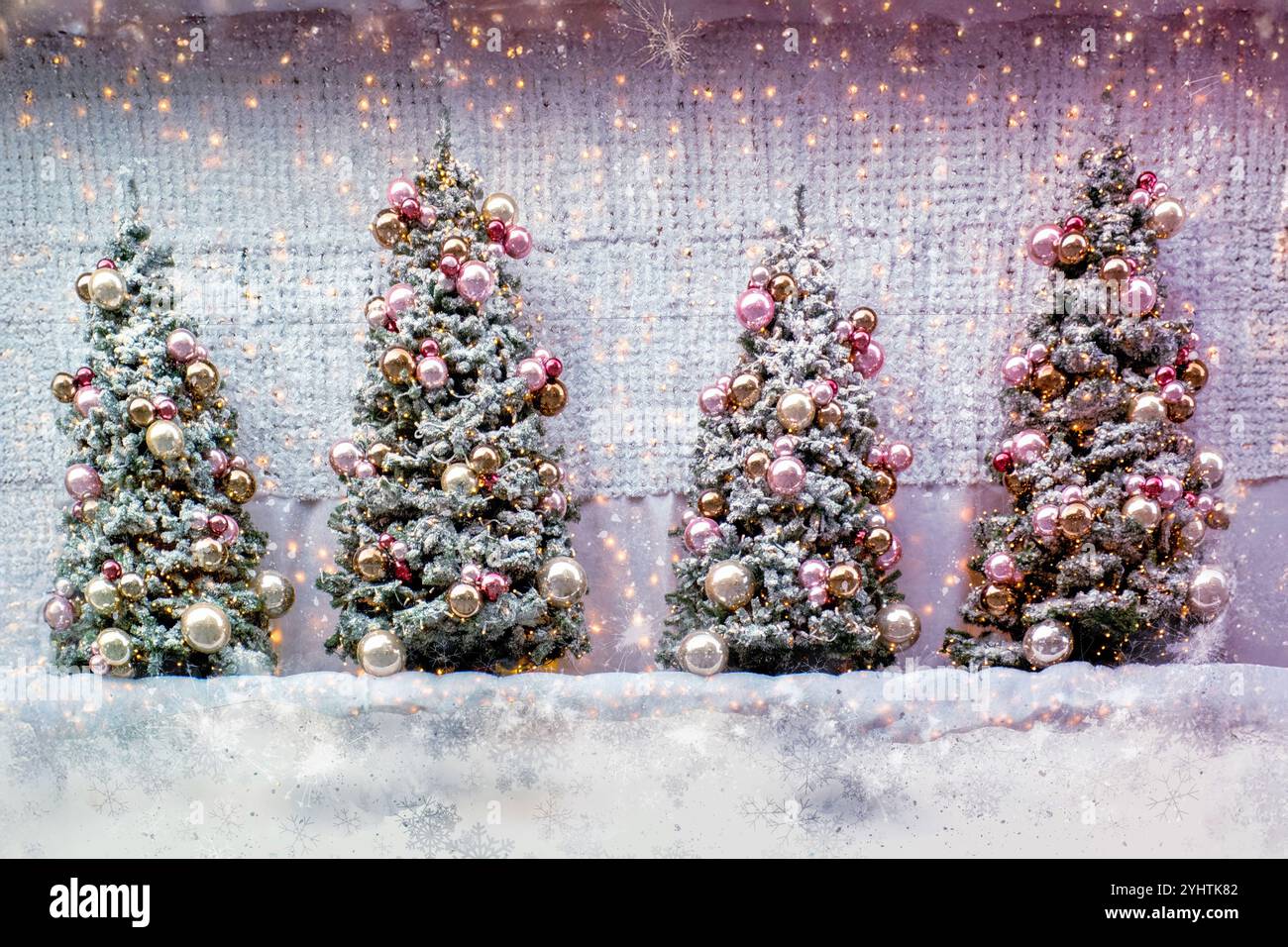 Quatre sapins de Noël enneigés ornés d'ornements dorés et roses se dressent dans une scène festive et enneigée avec des lumières scintillantes. Banque D'Images
