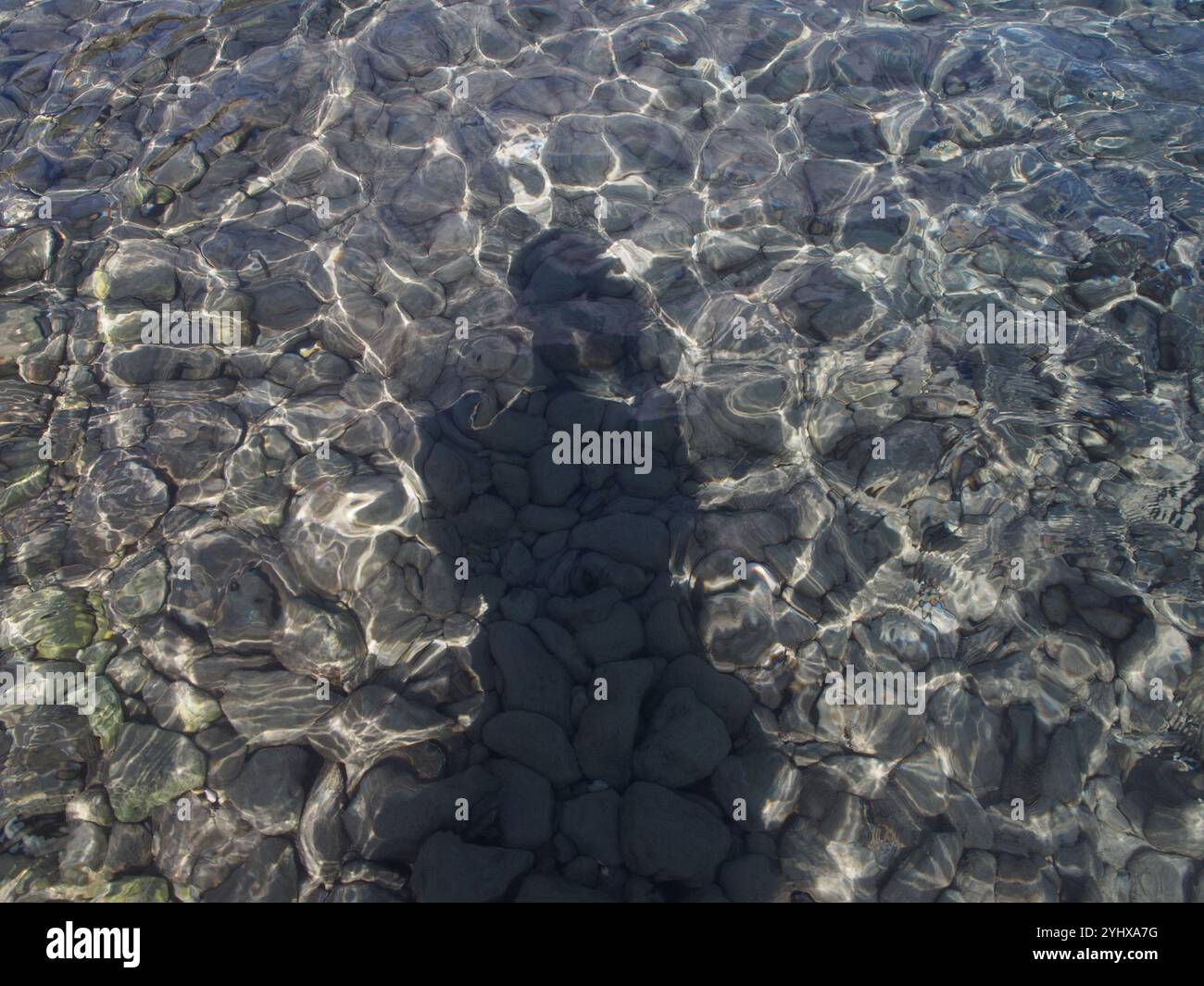 Ombre d'une personne projetée sur l'eau de l'océan peu profonde à une plage de galets à Corfou, Grèce. Concept : voyage solo, solitude, Banque D'Images