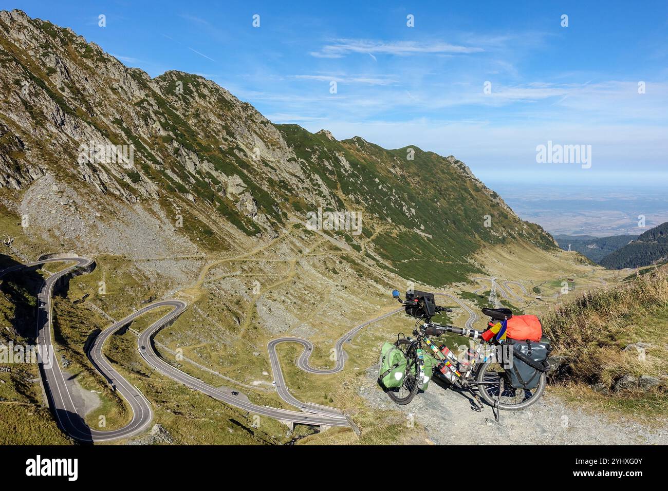 Vélo de randonnée chargé surplombant la route de montagne sinueuse de Transfăgărășan dans un paysage alpin isolé sous un ciel bleu clair Banque D'Images