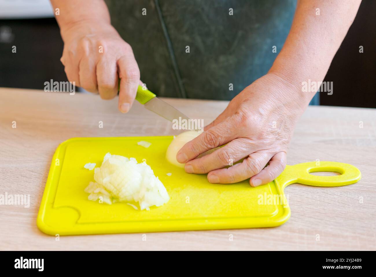 La femme coupe des oignons sur une planche à découper jaune. Elle utilise un couteau pour couper les oignons en petits morceaux Banque D'Images