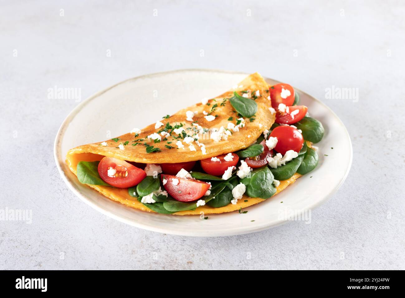 Omelette farcie avec tomates, fromage et épinards sur fond blanc. Banque D'Images