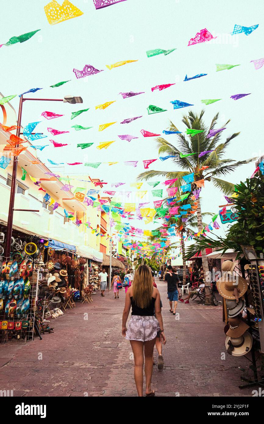 Des bannières colorées de picado papel flottent au-dessus d'une rue animée du marché avec des boutiques de souvenirs tandis qu'une femme s'éloigne de la caméra. Banque D'Images