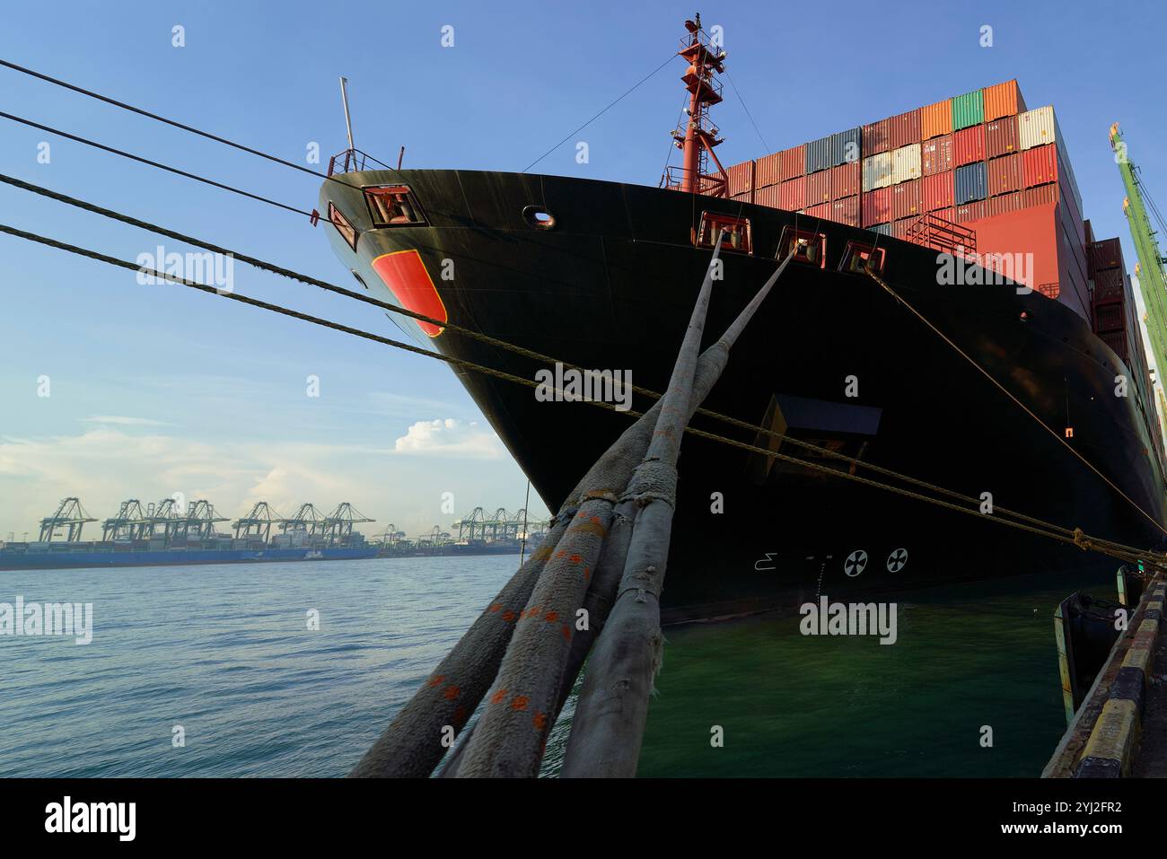 Navire de charge chargé de conteneurs amarrés à un quai commercial avec des grues en arrière-plan sous un ciel bleu, Busan, Corée Banque D'Images