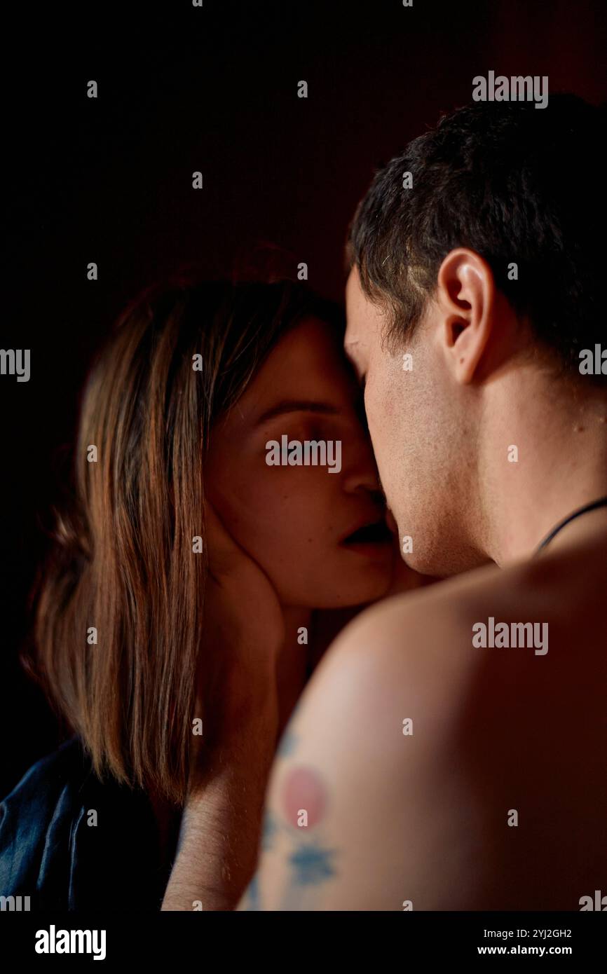 Moment intime d'un couple sur le point de s'embrasser, avec une femme touchant doucement le visage de l'homme sur fond rouge. Banque D'Images