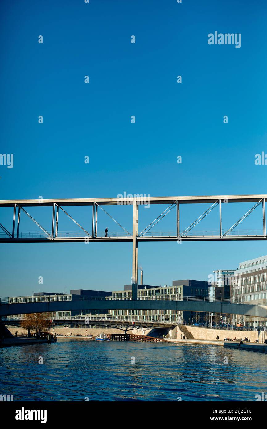 Pont piétonnier sur la rivière Spree avec une seule personne traversant, bâtiments modernes en arrière-plan sous un ciel bleu clair, Berlin, Allemagne Banque D'Images