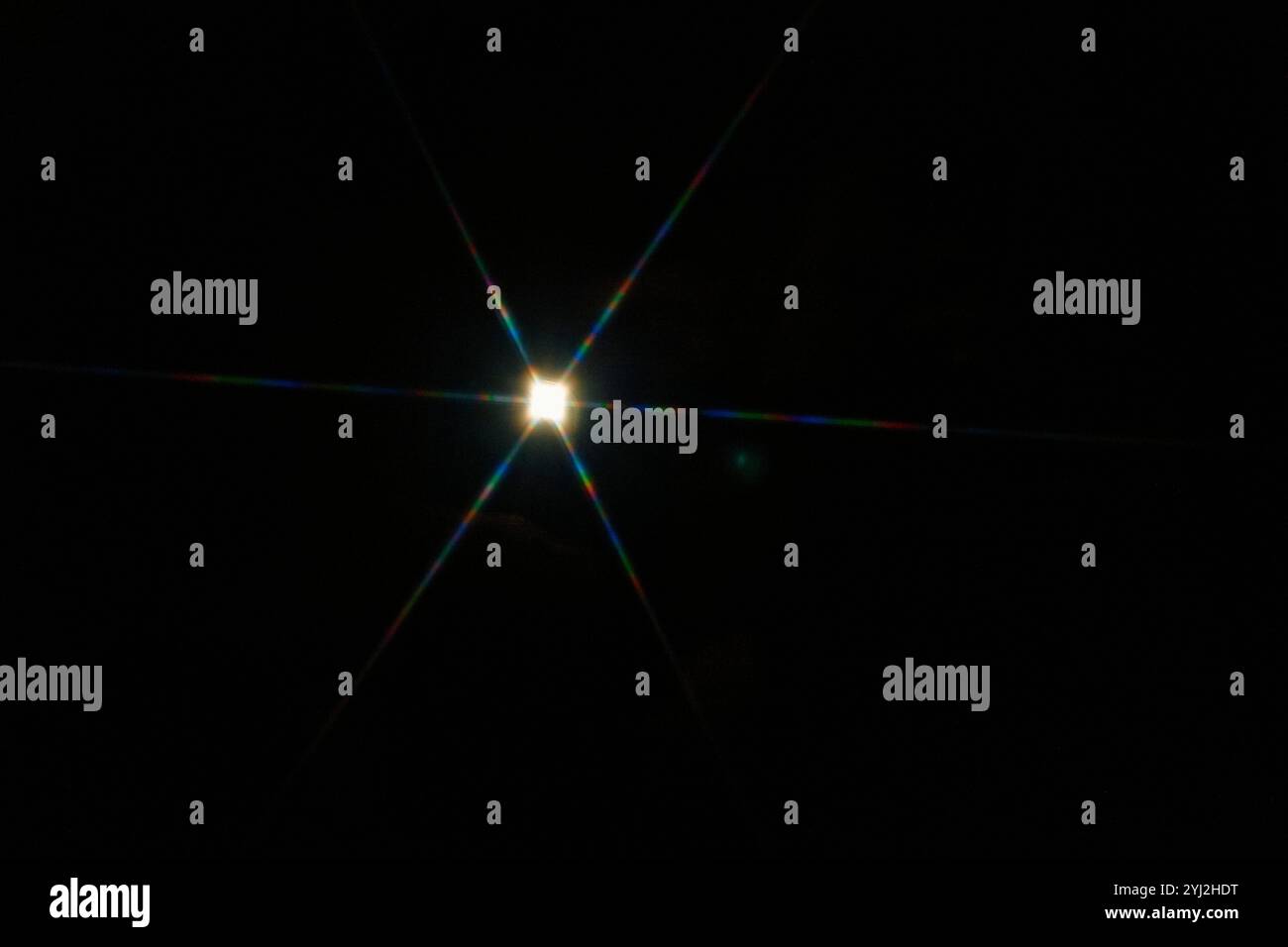 Effet lumineux Starburst lumineux avec des stries de diffraction colorées sur fond noir. Banque D'Images