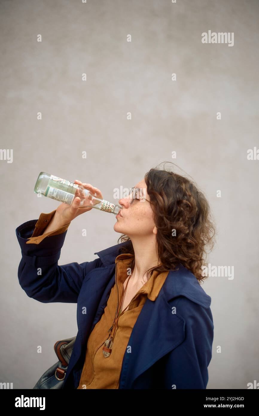 Femme dans une chemise bleue buvant dans une bouteille transparente. Banque D'Images