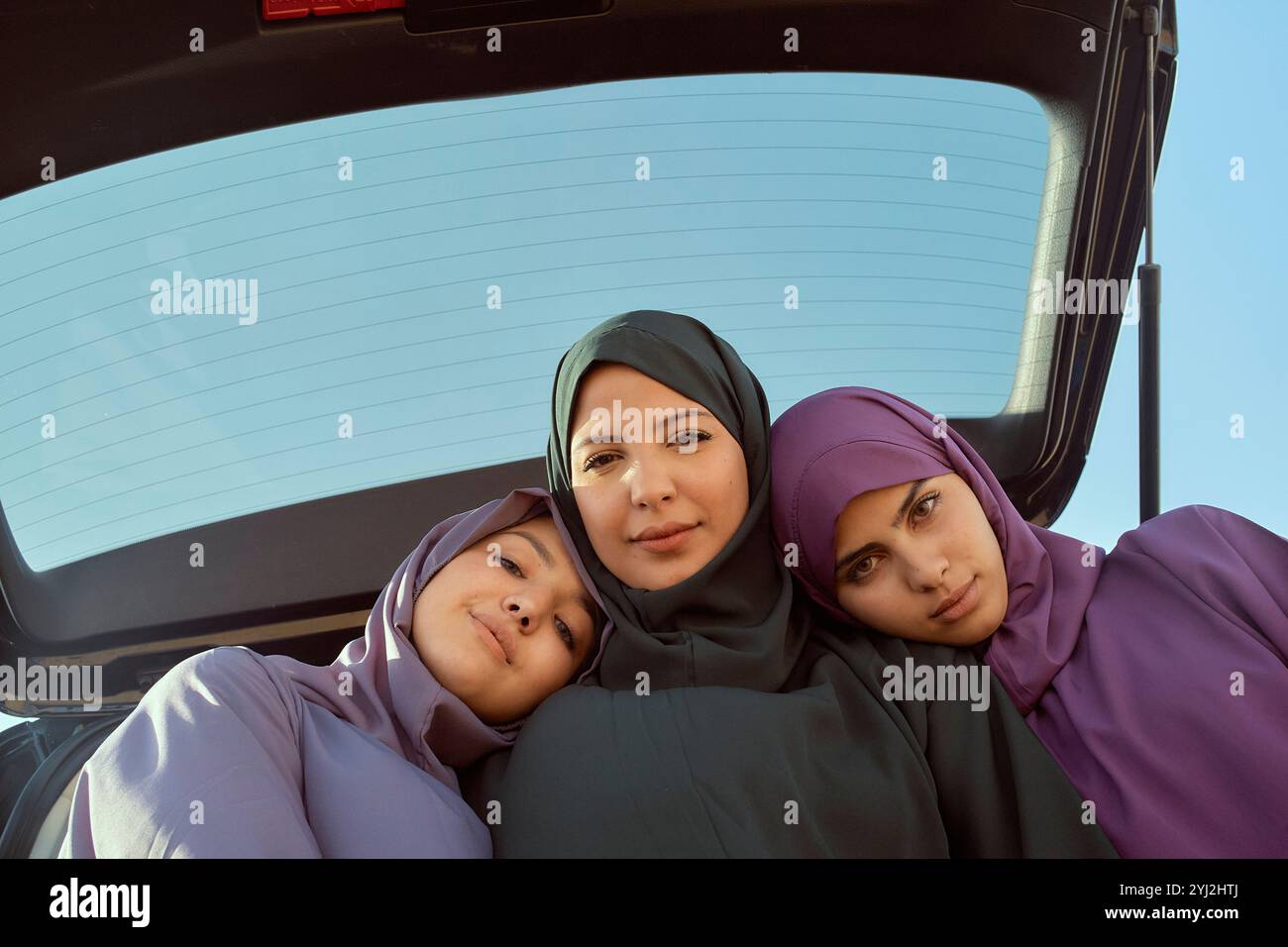 Trois femmes portant des hijabs souriants assis dans le coffre d'une voiture sous un ciel dégagé, Maroc Banque D'Images