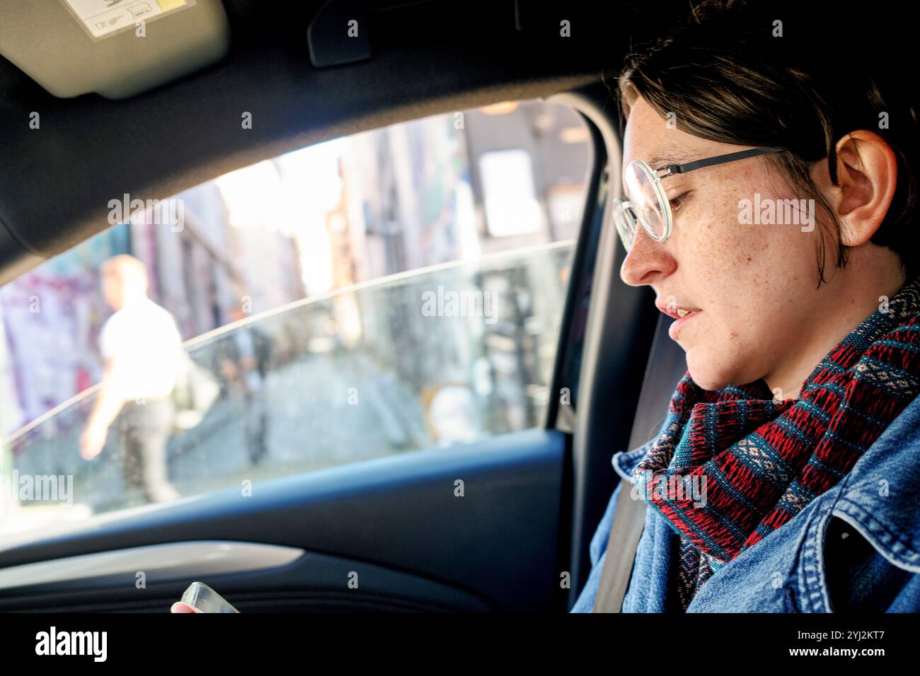 Une femme en lunettes regarde son smartphone tout en étant conduite à travers la ville Banque D'Images