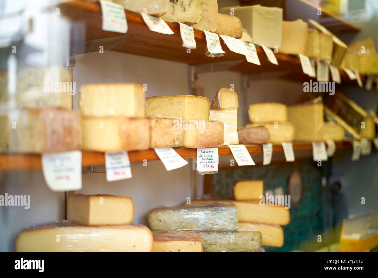 Assortiment de fromages sur des étagères en bois avec des étiquettes de prix dans une fromagerie, vu à travers la vitrine Banque D'Images