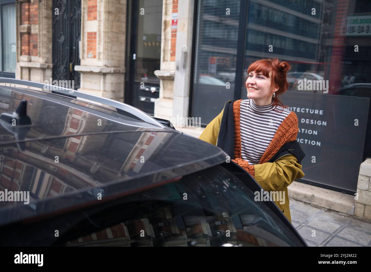 Femme souriante avec les cheveux roux regardant loin debout près d'une voiture dans une rue de la ville, Bruxelles, Belgique Banque D'Images