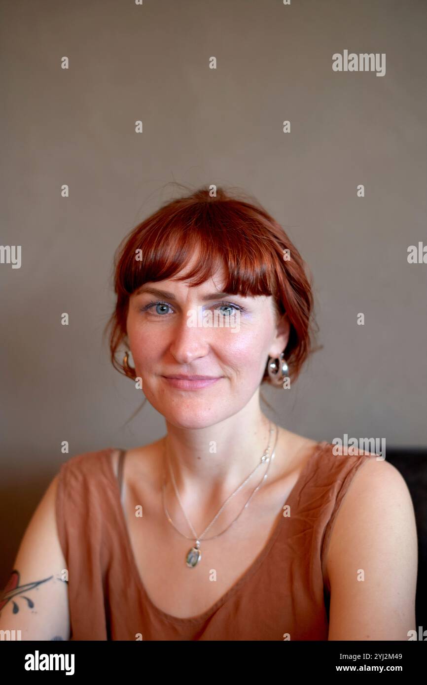 Femme souriante avec une frange rouge portant un haut marron et collier en argent sur un fond neutre. Banque D'Images