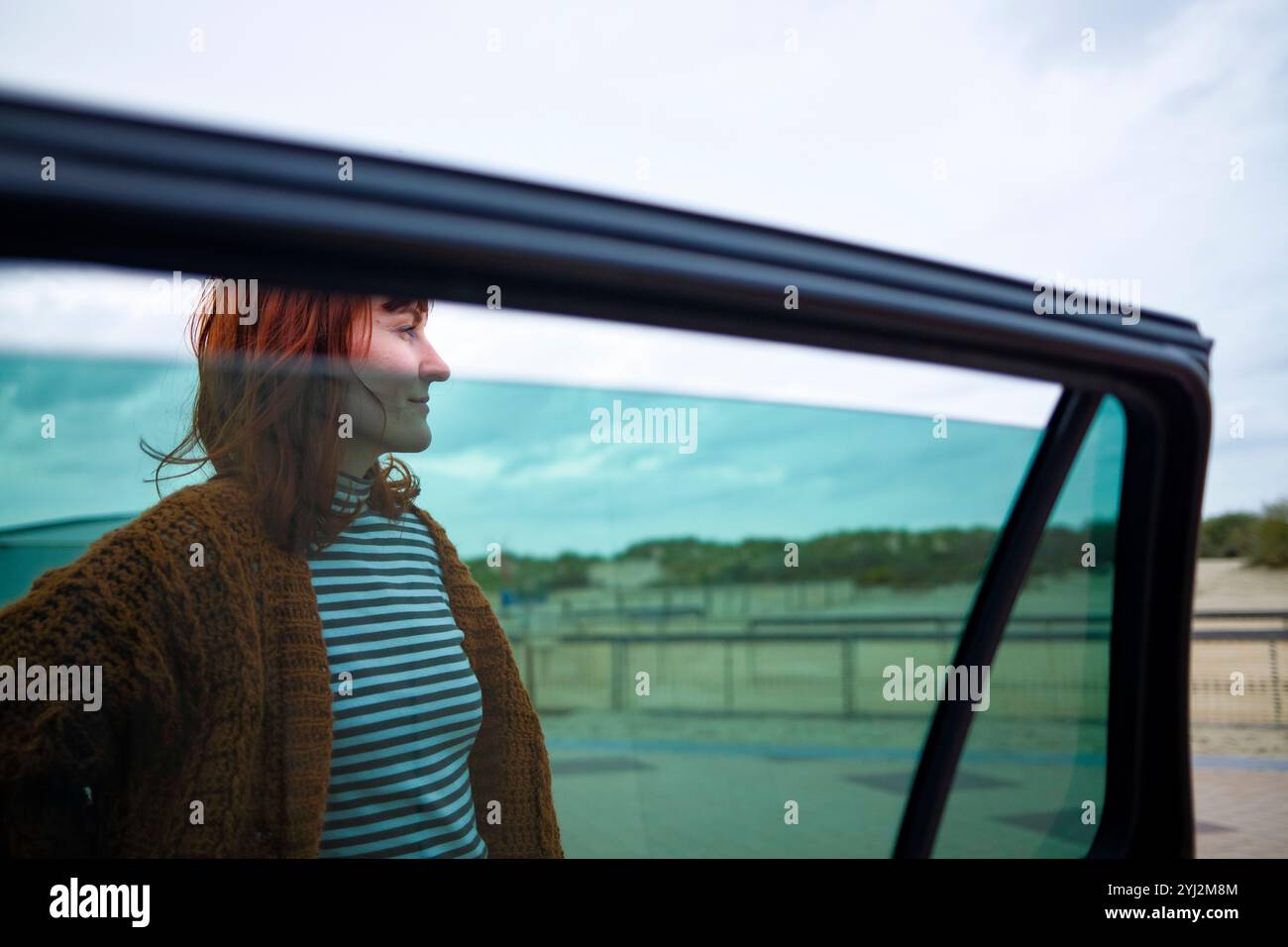 Femme souriante profitant d'une balade en voiture avec une vue sur le ciel et le paysage à l'extérieur de la fenêtre. Banque D'Images