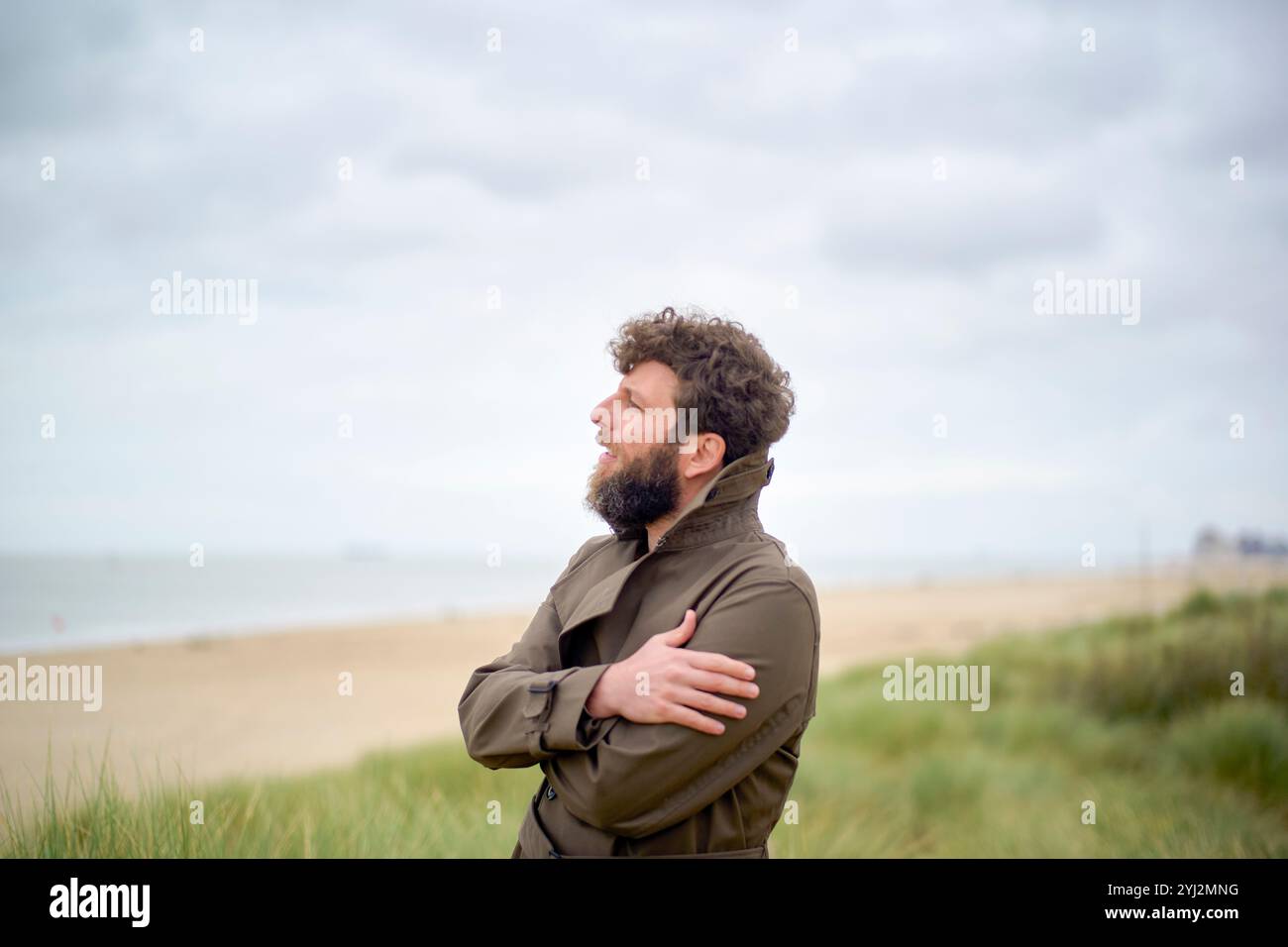 Un homme avec une barbe se tient sur une plage, regardant au loin, les bras croisés et une expression contemplative sur son visage, Belgique Banque D'Images