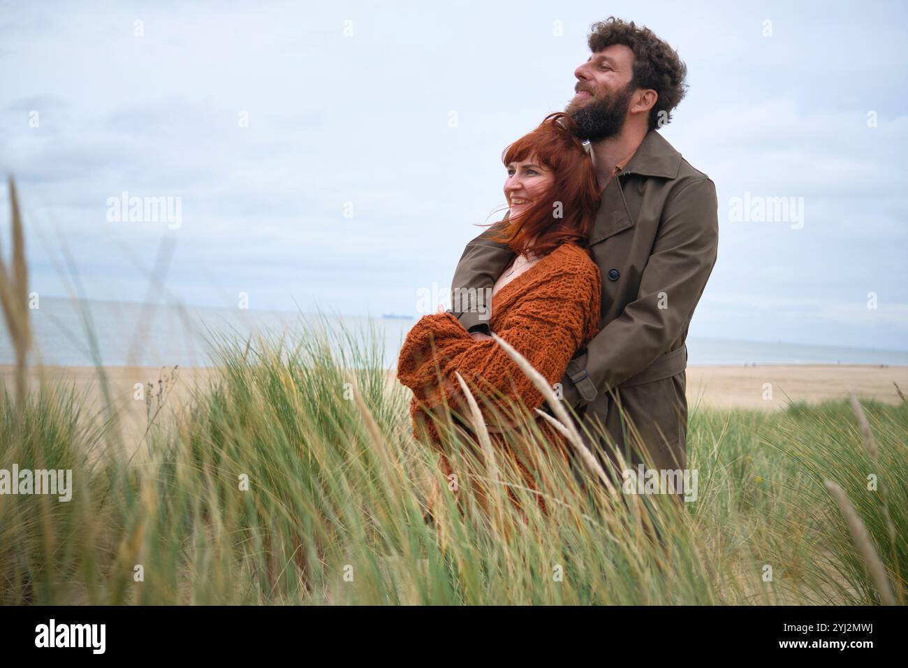 Un couple joyeux embrasse parmi de hautes herbes sur une plage de sable sous un ciel nuageux, Belgique Banque D'Images