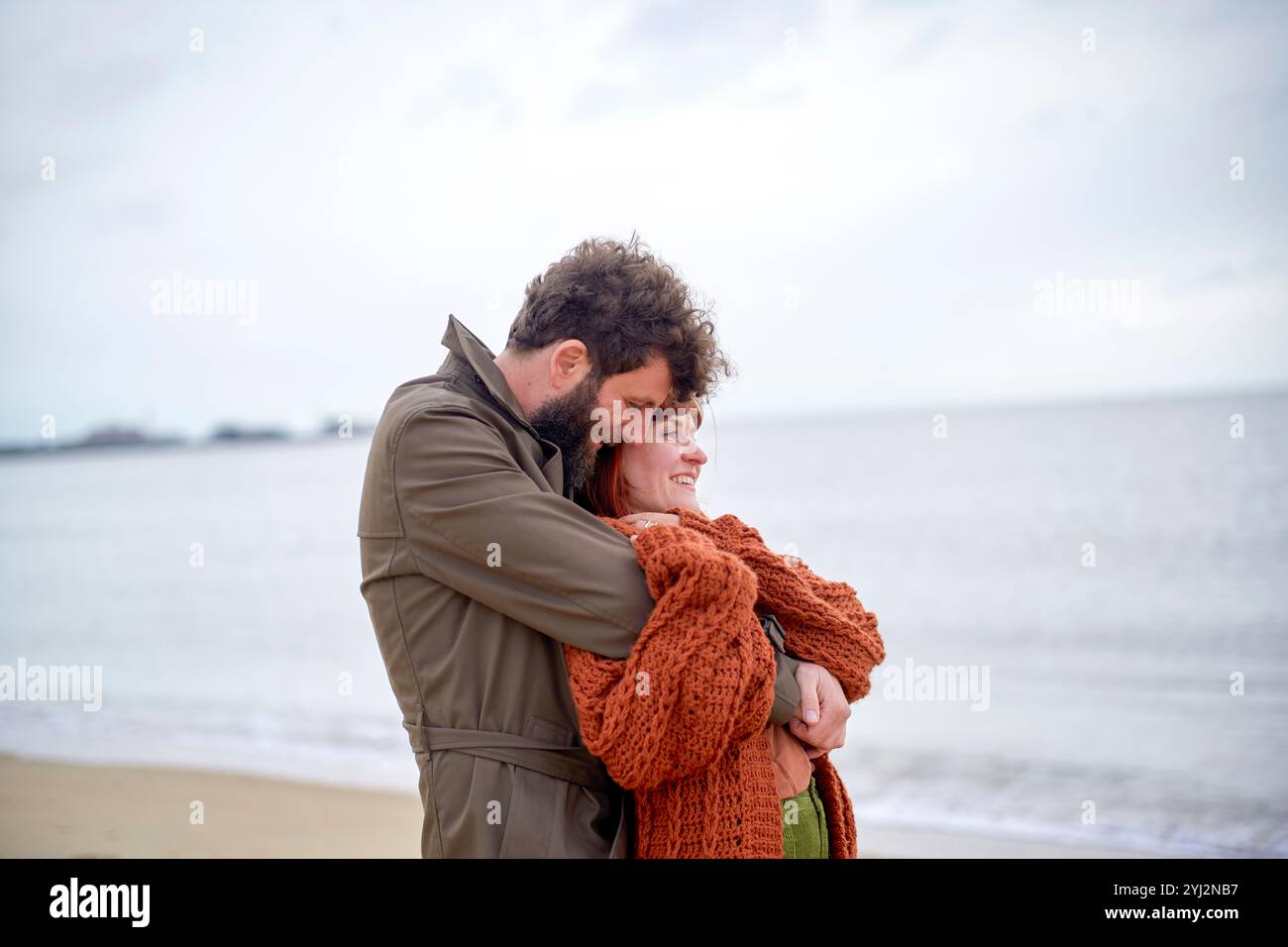 Couple embrassant sur une plage de sable au ciel couvert, affichant affection et chaleur, Belgique Banque D'Images