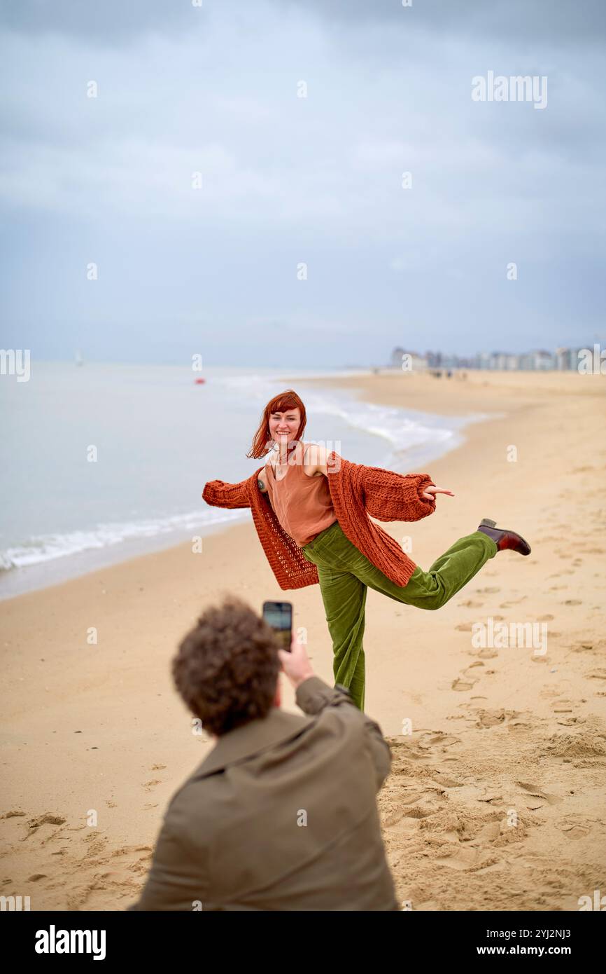 Personne posant pour une photo sur une plage de sable prise par un photographe accroupi au premier plan, Belgique Banque D'Images