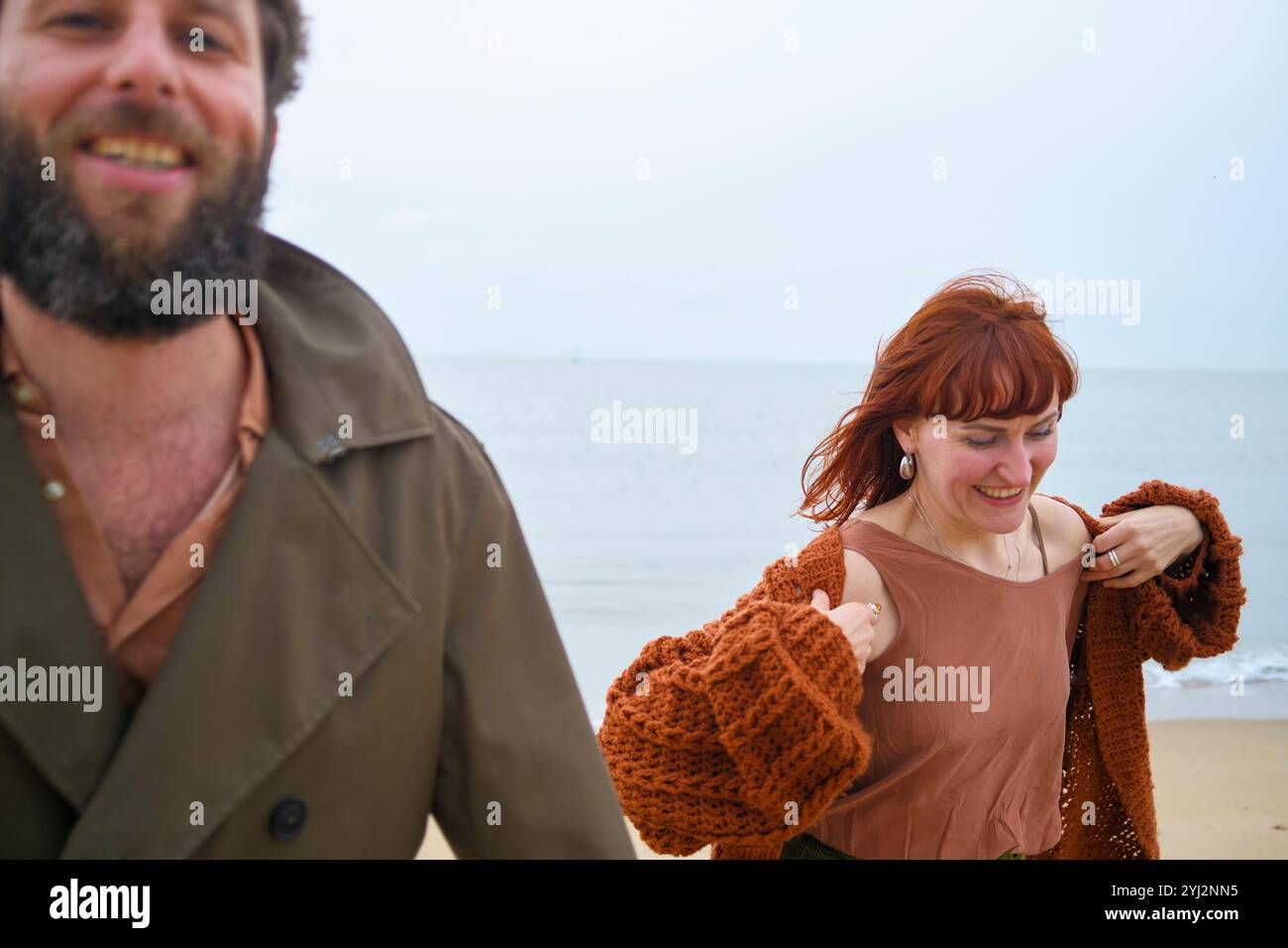 Homme barbu souriant et femme aux cheveux roux profitant d'une promenade sur la plage, Belgique Banque D'Images