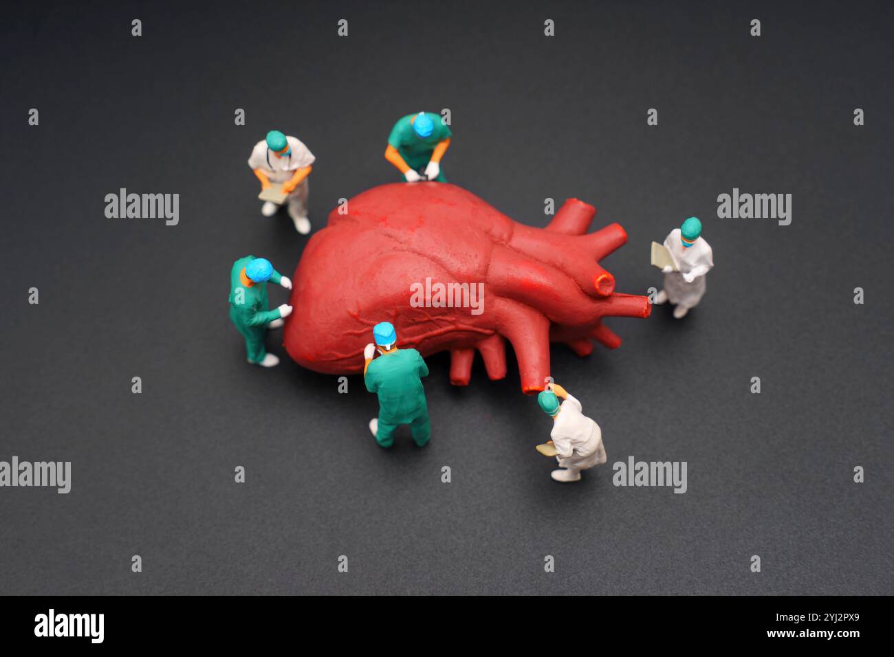 Modèle rouge vif d'un cœur humain entouré de figurines miniatures d'une équipe chirurgicale, vêtu de gommages et de casquettes chirurgicales, examinant et travaillant sur t Banque D'Images
