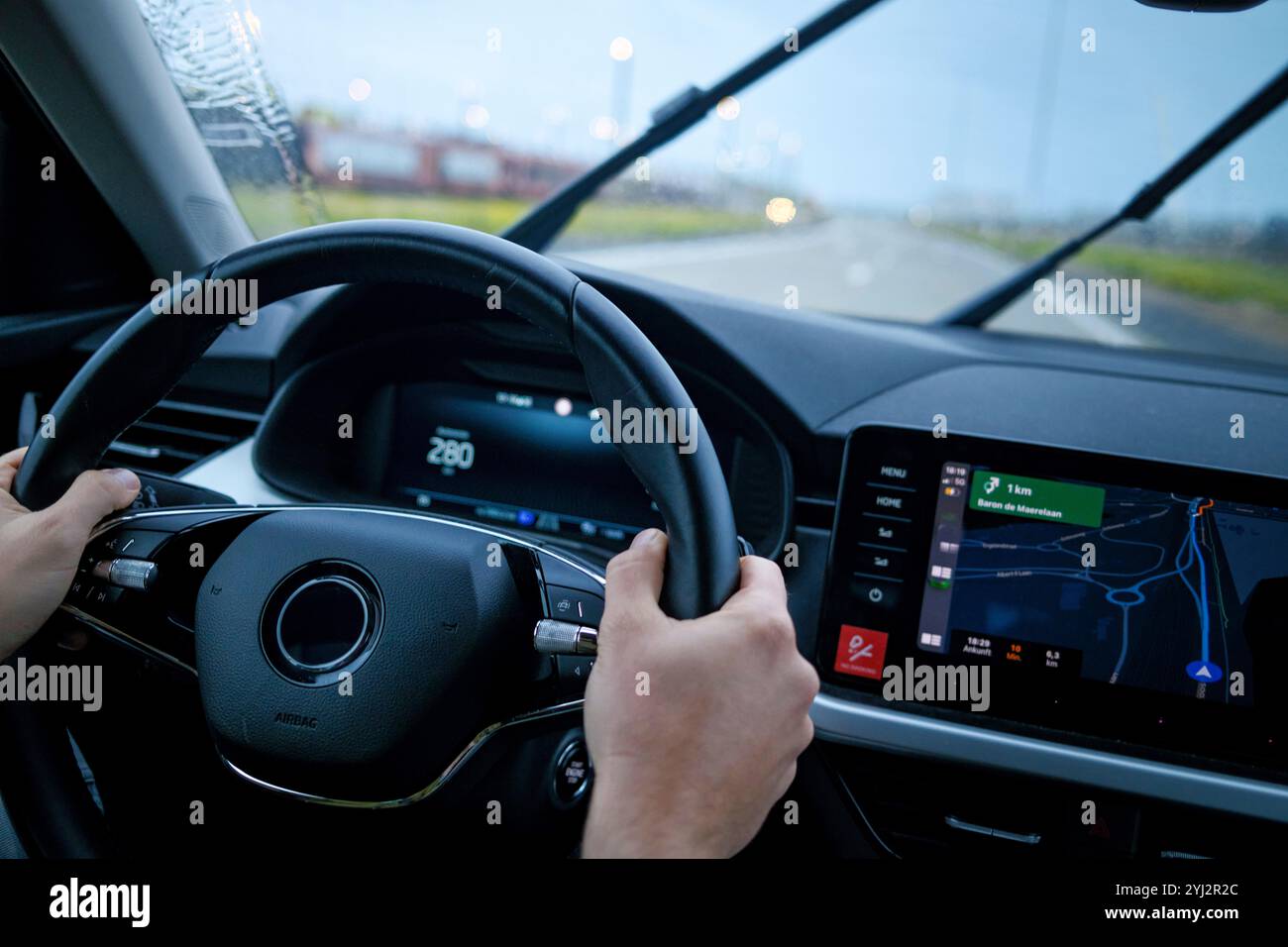 Mains tenant le volant d'une voiture avec un système de navigation sur le tableau de bord affichant une carte pendant un trajet. Banque D'Images