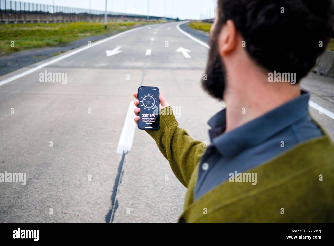 Homme tenant un smartphone affichant une application sbass sur une route vide. Banque D'Images