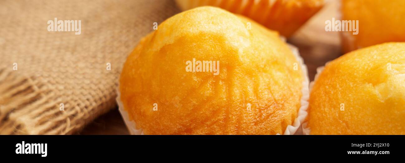 Muffins dorés sur surface en bois avec toile de jute rustique, soulignant la texture de cuisson fraîche et douce Banque D'Images