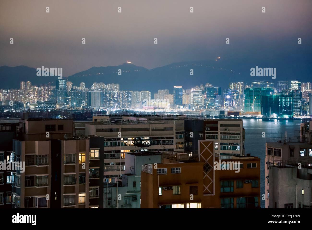 La ville de Hong Kong scintille la nuit, avec des bâtiments reflétant les lumières sur fond de montagnes lointaines. Banque D'Images