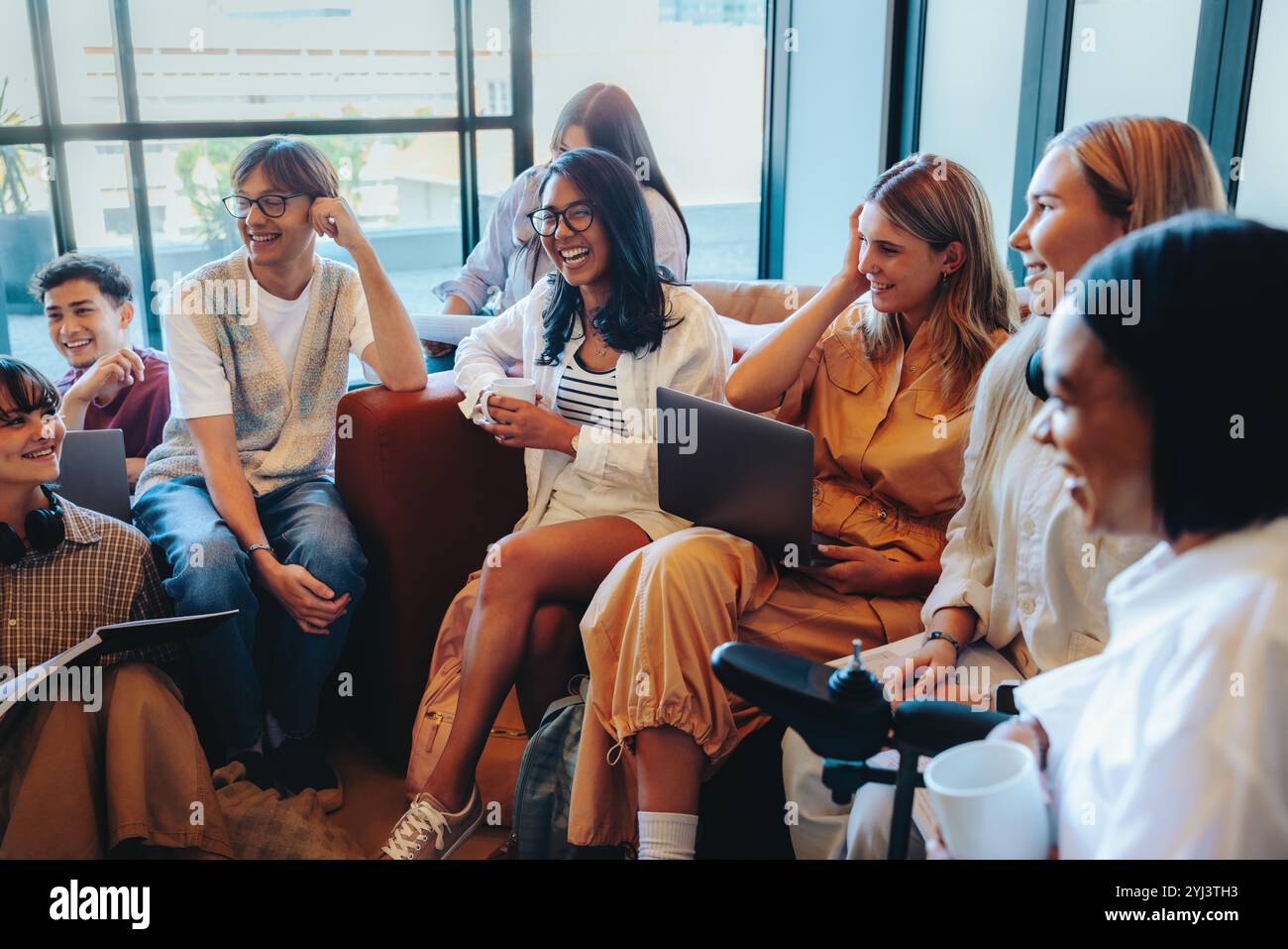 Un groupe multiculturel d'étudiants dans un cadre scolaire sont engagés dans une discussion animée, entouré d'ordinateurs portables et de cahiers dans une salle de classe moderne en Banque D'Images