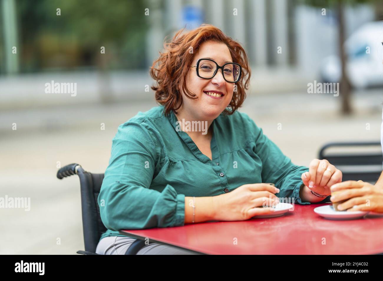 Femme handicapée en fauteuil roulant électrique buvant du café avec un ami assis dans une cafétéria extérieure dans la ville Banque D'Images