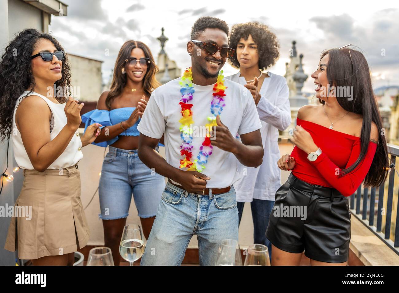 Heureux homme latin avec collier hawaïen dansant avec des amis dans la partie extérieure sur le toit Banque D'Images