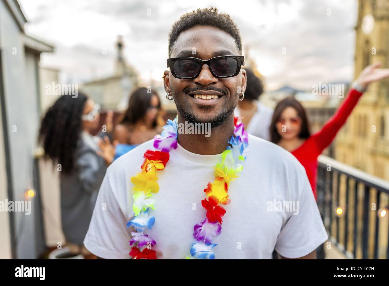 Portrait d'un homme latin en collier hawaïen souriant à la caméra avec des amis faisant la fête sur fond Banque D'Images