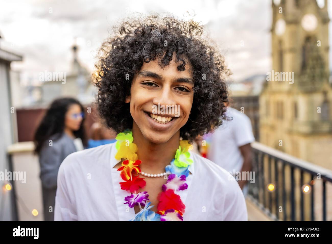 Homme heureux avec des cheveux bouclés et collier hawaïen souriant pendant la fête sur le toit Banque D'Images