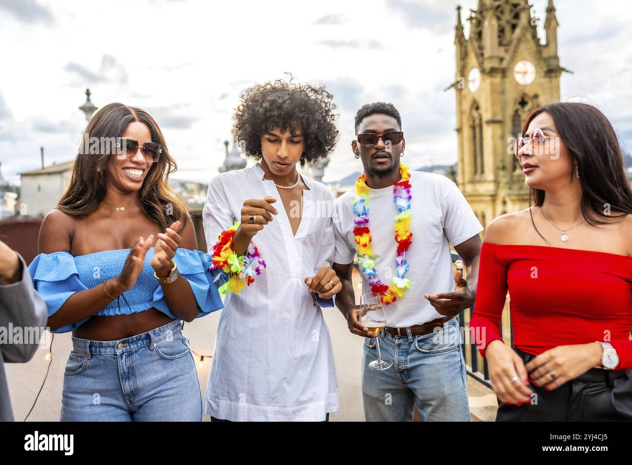 Amis multi-ethniques dansant habillés avec collier hawaïen dans une fête sur le toit au coucher du soleil Banque D'Images