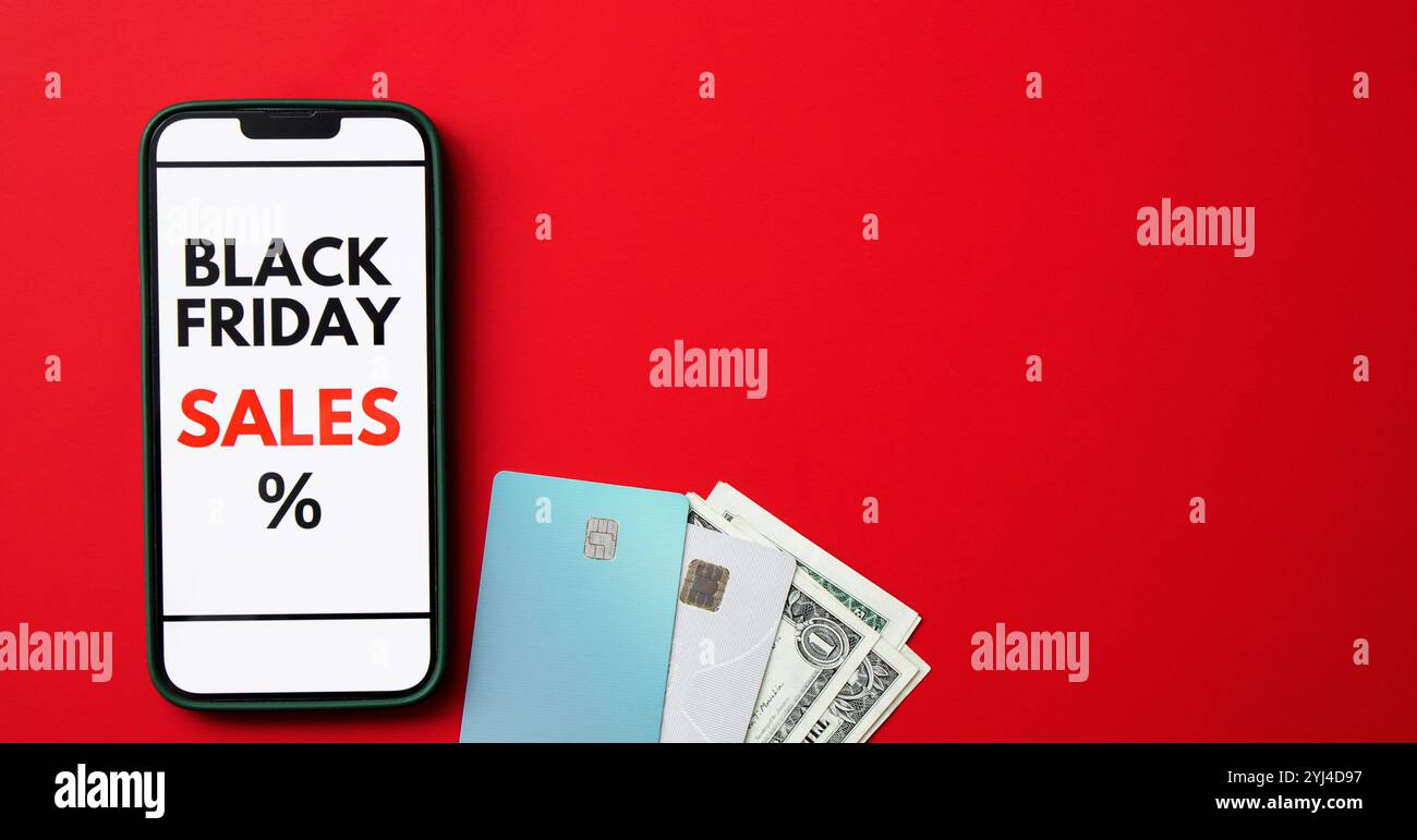 Vue de dessus d'un écran de smartphone affichant une vente en ligne Black Friday sur fond rouge avec des cartes de crédit et de l'argent Banque D'Images