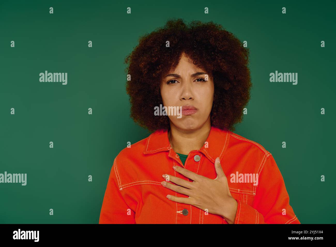 Une jolie jeune femme aux cheveux bouclés transmet une émotion profonde tout en étant habillée décontractée sur un fond vert. Banque D'Images