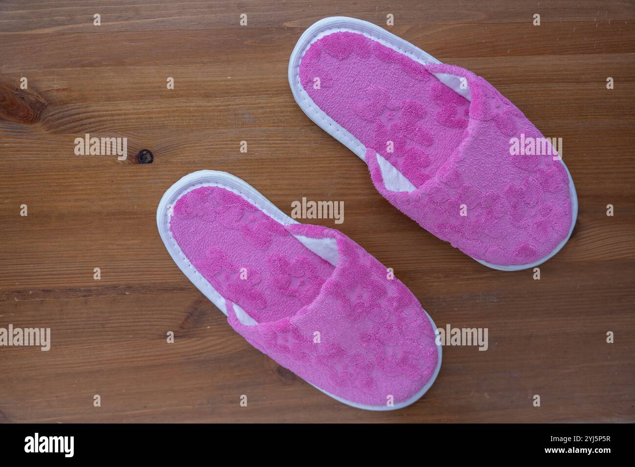 Une paire de chaussons roses reposant sur un plancher en bois, créant une atmosphère chaleureuse et accueillante dans la chambre. Banque D'Images