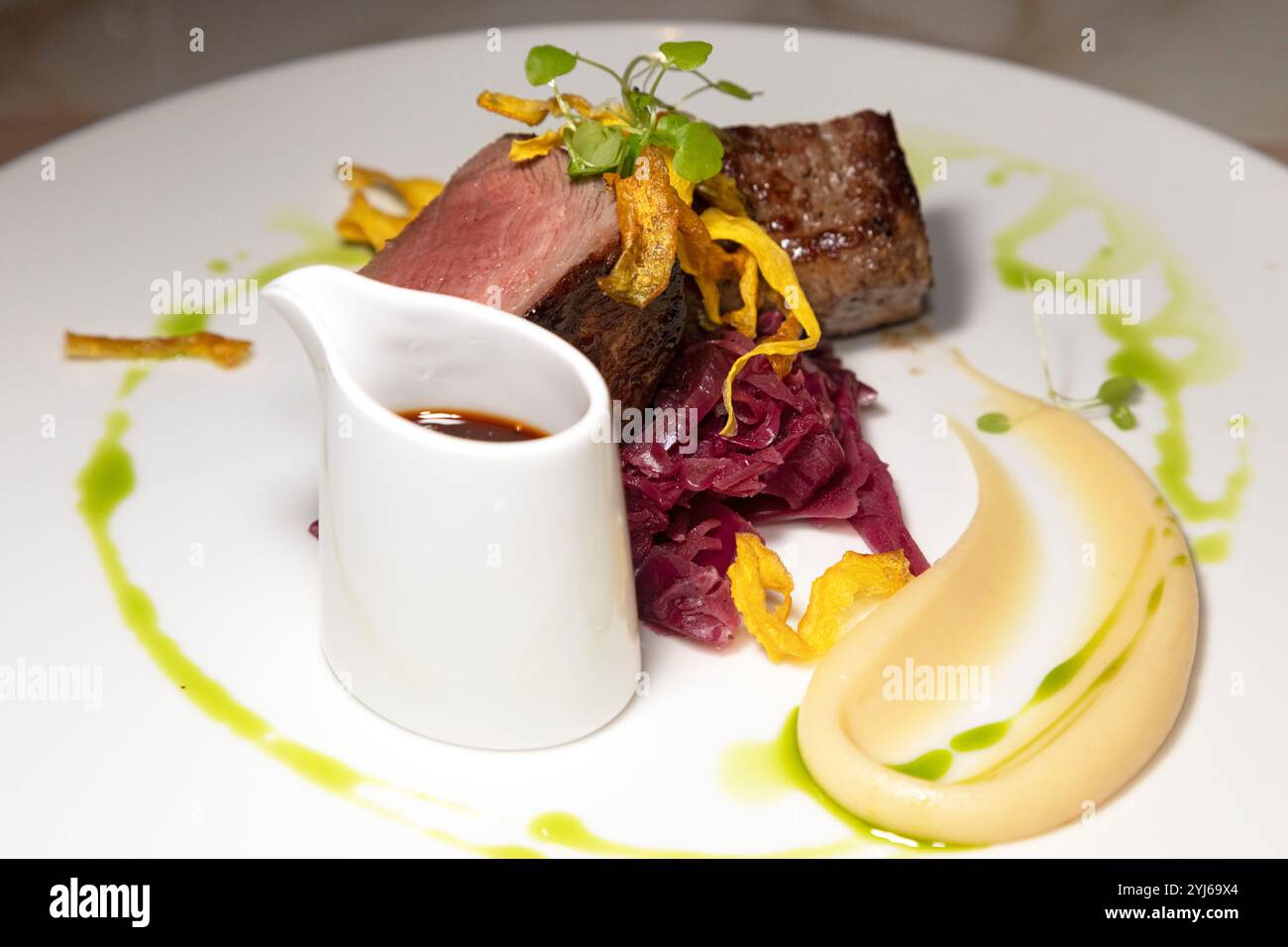 Longe de venaison servie avec panais croustillant, chou rouge braisé, purée de pommes de terre et un pichet de jus. Banque D'Images