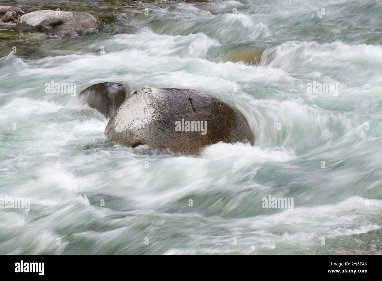 L'eau douce de la rivière de montagne coule au ralenti autour d'un gros rocher Banque D'Images