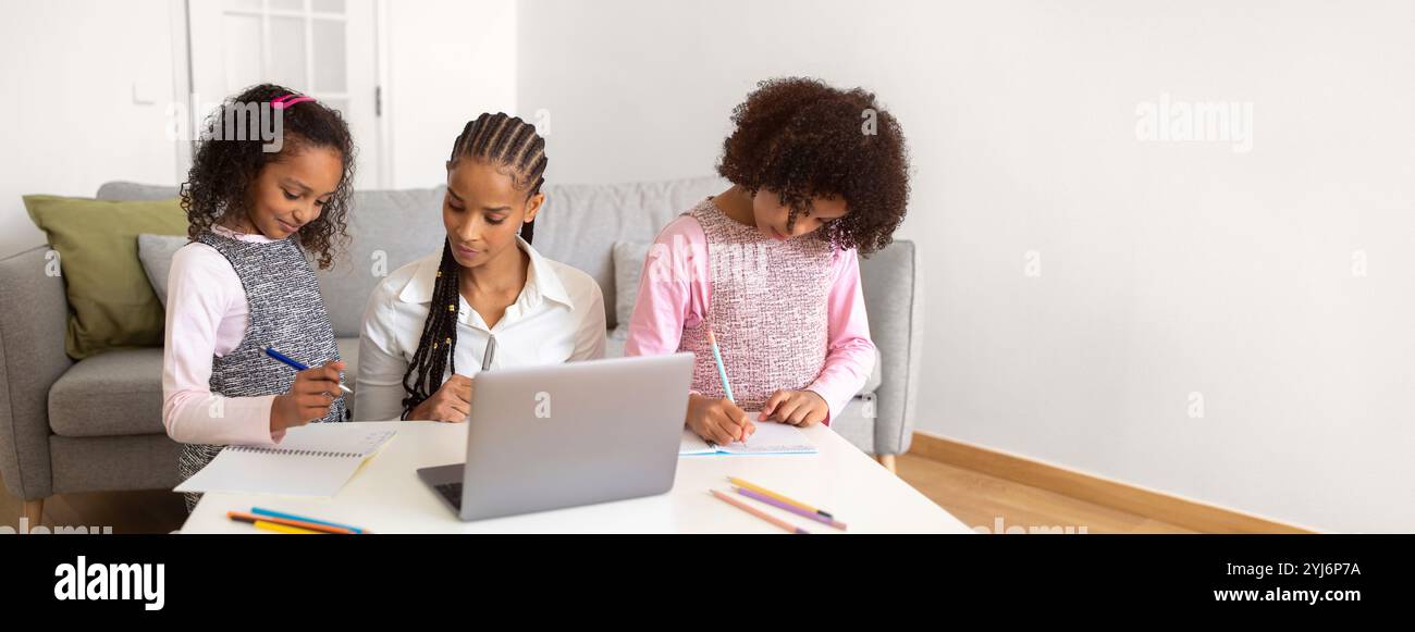 Mère afro-américaine assiste ses deux filles avec leurs devoirs dans un salon confortable, entouré d'une papeterie colorée et d'un ordinateur portable Banque D'Images