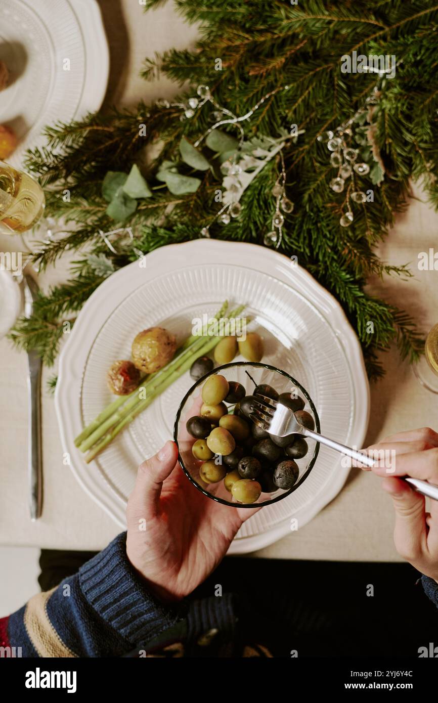 Plan haut vers le bas d'un homme méconnaissable assis à la table de fête et prenant des olives dans un bol en cristal Banque D'Images