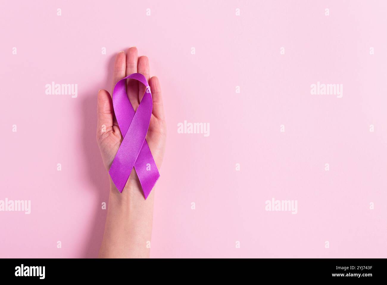 Ruban violet dans la main des femmes sur fond rose Banque D'Images