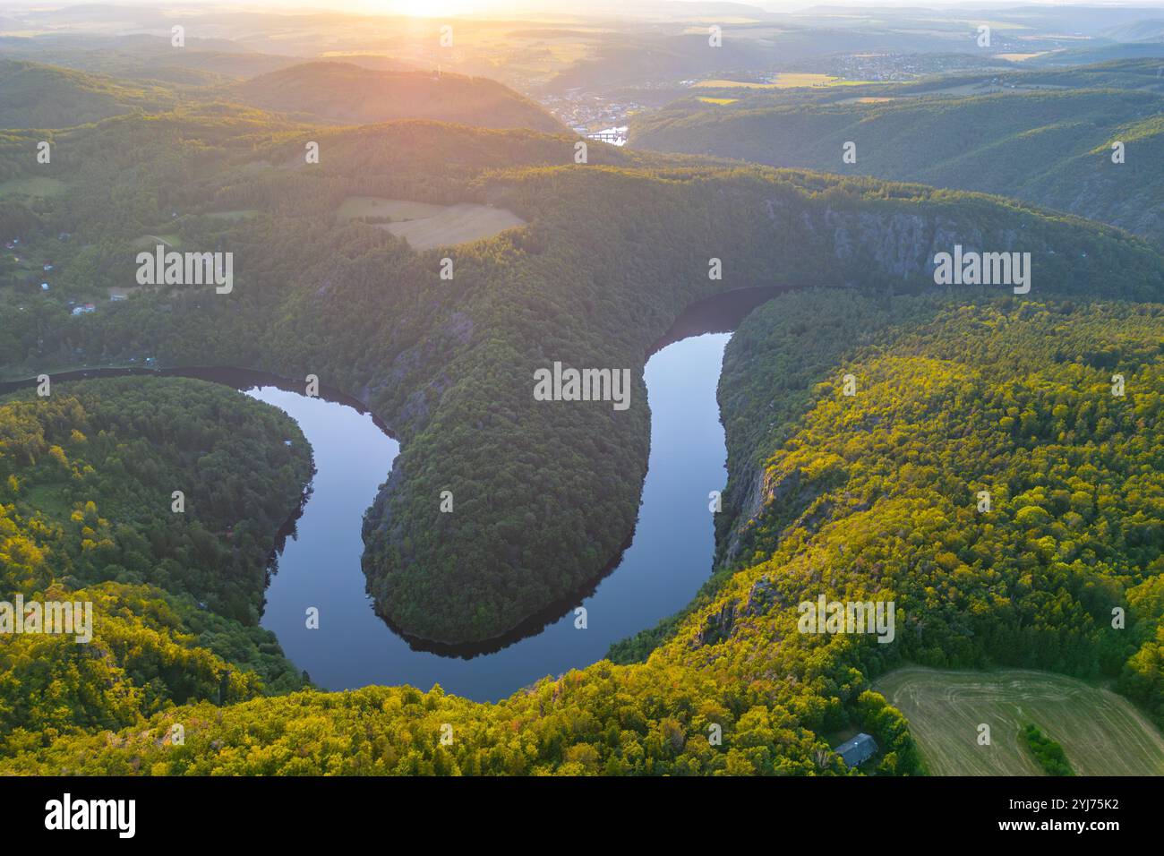 Alors que le soleil se couche, la rivière Vltava reflète des teintes vibrantes et encercle des collines verdoyantes en Tchéquie, créant une vue imprenable qui capture la beauté de la nature au crépuscule. Banque D'Images