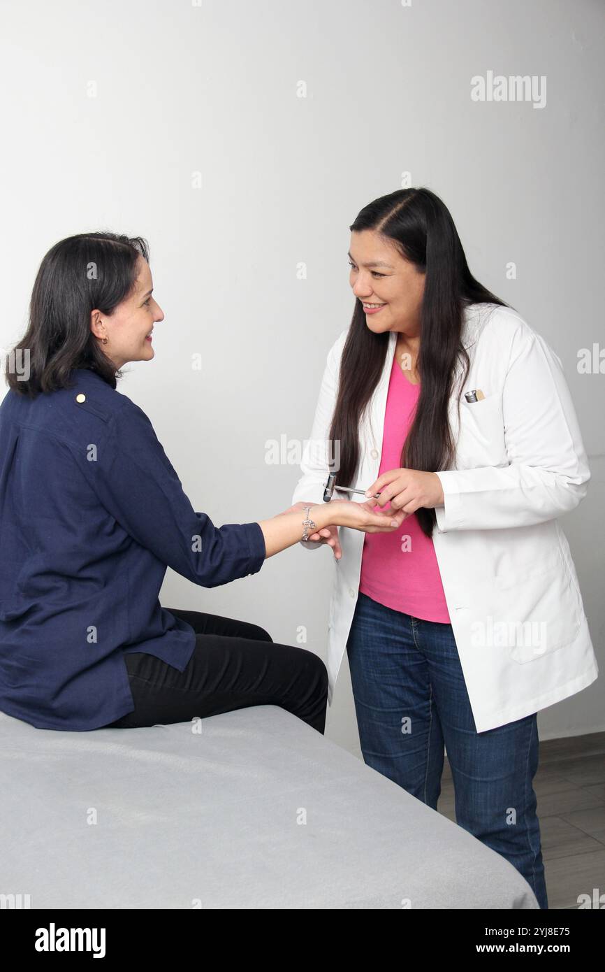 Latina Doctor femme assiste au patient dans le cabinet d'examen réflexe une partie de l'examen neurologique avec le marteau réflexe, frappe le tendon Banque D'Images