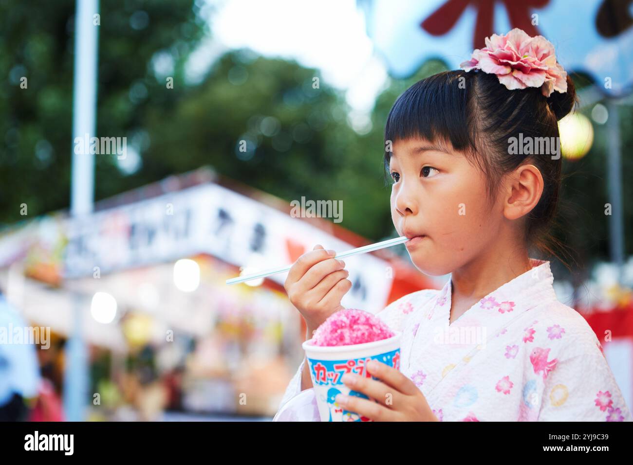 Fille en yukata mangeant de la glace rasée achetée dans un stand de festival Banque D'Images