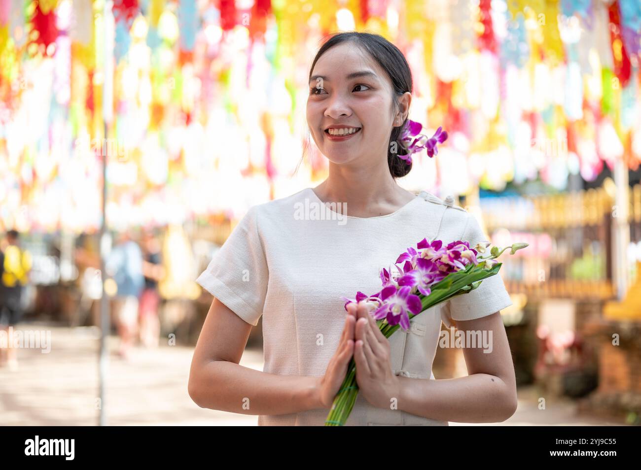 Une femme asiatique attrayante et souriante dans une robe traditionnelle thaïlandaise du Nord se tient dans un temple, tenant un bouquet d'orchidées avec des lanternes colorées dans le Banque D'Images